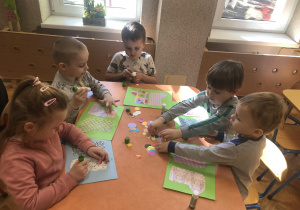 Dzieci ozdabiają skarpetkę wyciętą z papieru kolorowego kołami z origam.